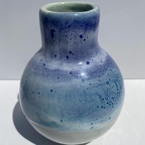 Könnte beinhalten: Eine kleine, handgefertigte Keramikvase mit rundem Körper und schmalem Hals. Die Vase hat einen Farbverlauf von Blautönen, der von einem hellblauen Sockel zu einem tiefen Blau an der Spitze übergeht. Die Oberfläche hat eine gesprenkelte Textur.