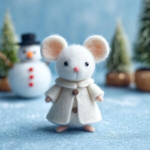 May include: A handcrafted white felt mouse wearing a cream-colored coat with two brown buttons. The mouse has large, round ears and a pink nose. A snowman and miniature Christmas trees are in the background.