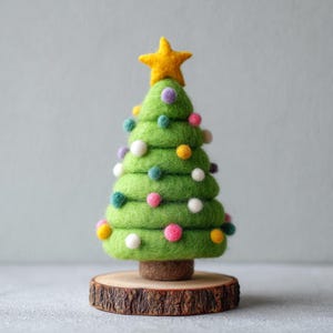 May include: A handcrafted, green felt Christmas tree with colorful pom-pom ornaments and a yellow star topper. The tree sits on a small, round wooden base, perfect for holiday decor. The tree is approximately 5 inches tall.