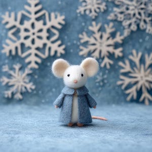 May include: A handcrafted felt mouse figurine with large, round ears and a light blue coat. The mouse stands on a blue surface, with white snowflake cutouts in the background. The figurine has a small pink tail.