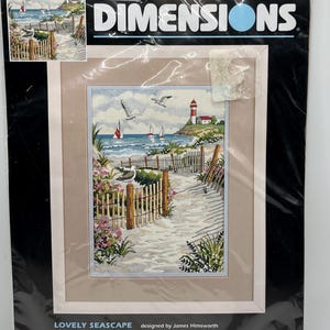 May include: A Dimensions no count cross stitch kit titled Lovely Seascape featuring a coastal scene with a lighthouse, sailboats, seagulls, and a wooden fence along a sandy path. The package includes 14 count ivory Aida, thread, and needle.
