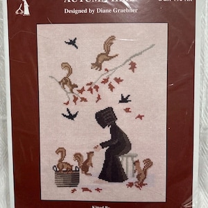 May include: Cross-stitch kit titled "AUTUMN HELP" designed by Diane Graebner. The design features a person feeding squirrels, with autumn leaves and birds. The kit is packaged in a clear plastic sleeve.