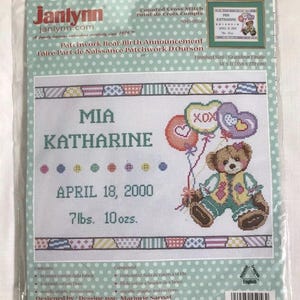 May include: A Janlynn counted cross-stitch kit for a Patchwork Bear Birth Announcement. The design features the name MIA KATHARINE, birth date April 18, 2000, and weight 7lbs. 10oz. The finished size is 14 x 11 inches.
