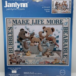 May include: A counted cross-stitch kit by Janlynn featuring a design of teddy bears in a bathtub with bubbles. The kit includes fabric, floss, a needle, and instructions. The design size is 18 x 14 inches.