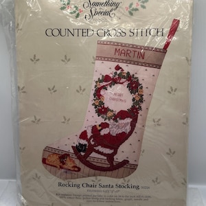 May include: A counted cross stitch kit for a Christmas stocking. The design features Santa Claus in a rocking chair, a wreath, and the text "Merry Christmas". The stocking is labeled "Martin" and measures 12" x 17".