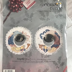 May include: A counted cross-stitch kit for door knob decor. The kit includes two round designs with angel motifs, the words "Joy" and "Noel", and decorative lace trim. The package reads "DOORKNOB DECOR" and "Angels".