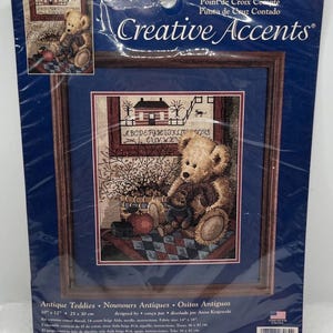 May include: Counted cross stitch kit featuring a framed image of antique teddy bears. The artwork includes a large teddy bear holding a smaller one, with a house and alphabet in the background. The kit measures 10" x 12" (25 x 30 cm).