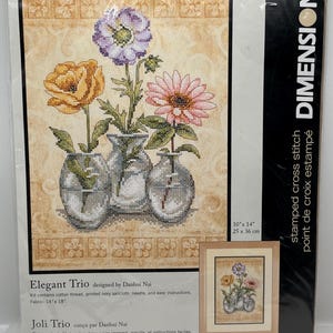 May include: A cross-stitch kit featuring a floral design titled "Elegant Trio." The artwork showcases three vases with colorful flowers: a yellow rose, a pink daisy, and a purple anemone. The kit includes cotton thread and measures 10" x 14".