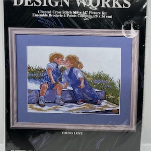 May include: Design Works counted cross stitch picture kit titled Young Love, measuring 11 inches by 14 inches. The packaging features an illustration of two children sitting on a stone wall, wearing blue overalls, with a blue mat and frame.