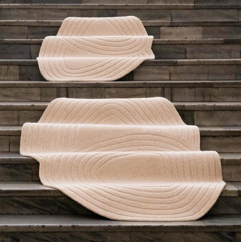 May include: Beige stair treads with a textured, wave-like pattern. The treads are placed on stone steps, creating a soft contrast with the hard surface. The design adds a touch of warmth and style to the staircase.