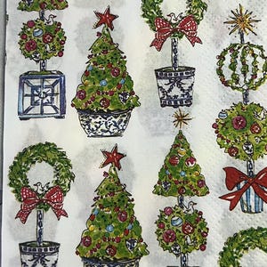 Peut inclure: Une serviette blanche avec un motif répété d'arbres de Noël, de couronnes et de topiaires décoratifs bleus et verts. Les arbres sont ornés de décorations et surmontés d'étoiles. Des nœuds rouges ajoutent une touche festive.