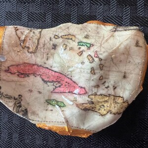 Może przedstawiać: Ręcznie wykonana, postarzana mapa wysp karaibskich, z Kubą w kolorze różowym i innymi wyspami w kolorze zielonym i żółtym. Mapa znajduje się na teksturowanej, kremowej powierzchni ze złotą obwódką i białym sznurkiem.