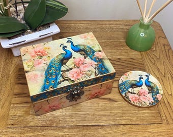 Caja rectangular de madera decorada a mano en estilo decoupage. Presenta un diseño de pavo real en rosa, azul y crema.