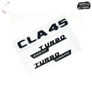 May include: Black CLA 45 Turbo and 4MATIC Turbo car emblem stickers on white backing. The stickers are hand made. The CLA 45 emblem is at the top, with Turbo and 4MATIC Turbo below. The stickers are for car enthusiasts.