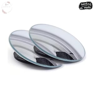 May include: Two oval-shaped, clear acrylic mirrors with a reflective surface, resting on black bases. The mirrors have a slight curve and are displayed against a white background. The image includes the text "hand made".