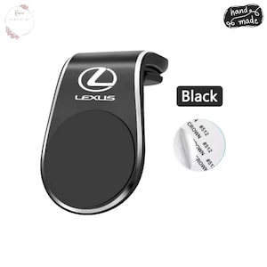 Puede incluir: Soporte negro para teléfono de coche con borde plateado y el logotipo de Lexus. El soporte tiene un área magnética circular y una pinza para sujetar a una rejilla de ventilación del coche. Se muestra la palabra "Black".