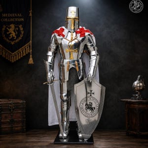 : A full suit of polished steel plate armor featuring a flat-topped helmet with a gold cross, a white cape with red crosses, a gold cross emblem on the chest, a long steel sword, and a large shield with a circular knight illustration.