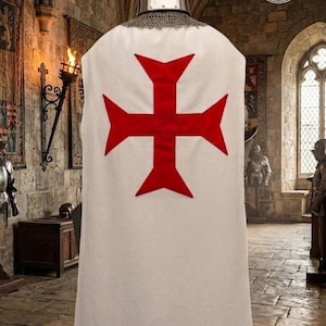 K&ouml;nnte beinhalten: Ein wei&szlig;er &auml;rmelloser Waffenrock mit einem gro&szlig;en roten Tatzenkreuz auf der R&uuml;ckseite, getragen &uuml;ber einer metallischen Kettenhaube und einem silberfarbenen zylindrischen Helm. Das Kleidungsst&uuml;ck wird auf einer Puppe in einem Raum aus Stein pr&auml;sentiert.