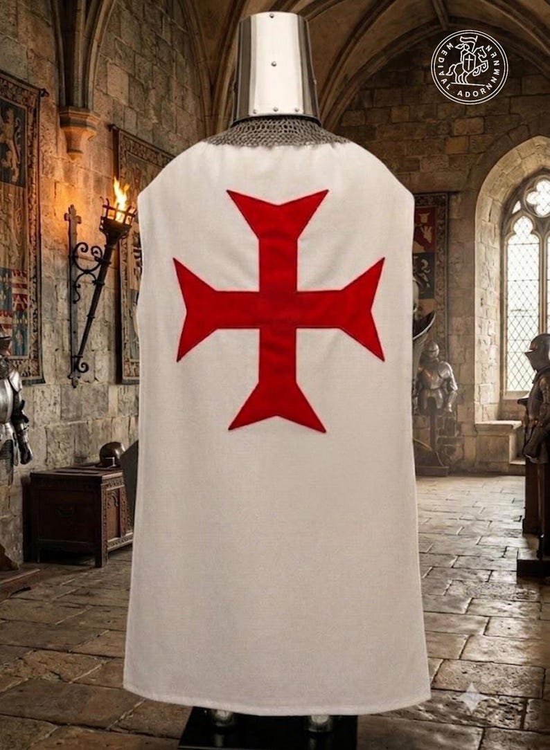 K&ouml;nnte beinhalten: Ein wei&szlig;er &auml;rmelloser Waffenrock mit einem gro&szlig;en roten Tatzenkreuz auf der R&uuml;ckseite, getragen &uuml;ber einer metallischen Kettenhaube und einem silberfarbenen zylindrischen Helm. Das Kleidungsst&uuml;ck wird auf einer Puppe in einem Raum aus Stein pr&auml;sentiert.