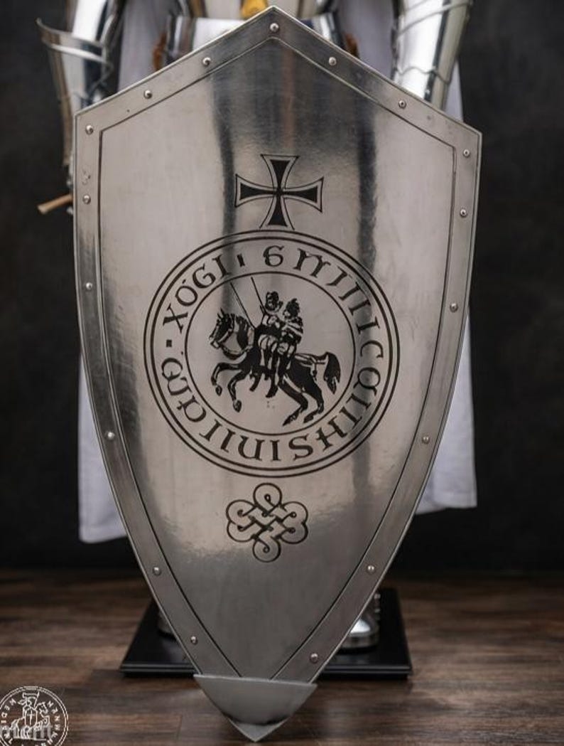 K&ouml;nnte beinhalten: Ein polierter, silberfarbener Metallschild mit schwarzer Gravur. Der Schild zeigt oben ein Kreuz, in der Mitte ein kreisf&ouml;rmiges Emblem mit einem berittenen Ritter und unten ein dekoratives Knotensymbol, umrandet von Nieten am Rand.