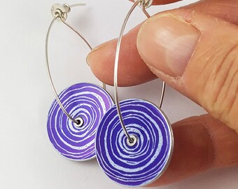 May include: A pair of silver hoop earrings with purple and white swirl designs. The earrings are made of metal and have a simple, elegant design.