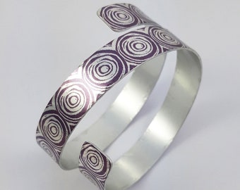 May include: A silver bangle bracelet with a purple and white concentric circle pattern.