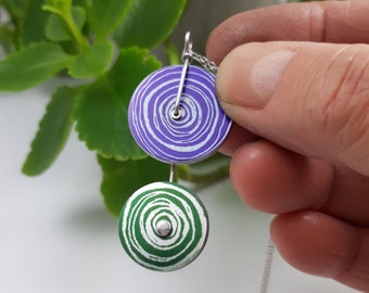 May include: A silver chain necklace with two round pendants. The top pendant is purple with white swirls and the bottom pendant is green with white swirls.