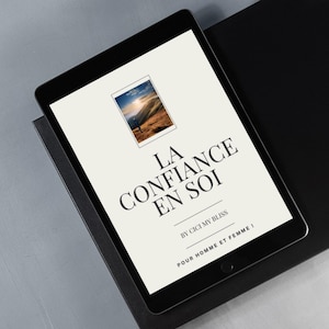 Peut inclure: Une tablette noire affiche une couverture de livre avec le titre "LA CONFIANCE EN SOI" en gros caractères. La couverture comprend une petite image d'une personne sur une montagne et le texte "BY CICI MY BLISS".