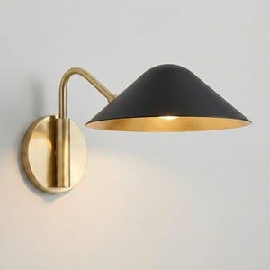 May include: A modern wall sconce with a black conical shade and a gold interior. The fixture has a brass-colored arm and a circular base. The design is minimalist and elegant, suitable for various interior styles.