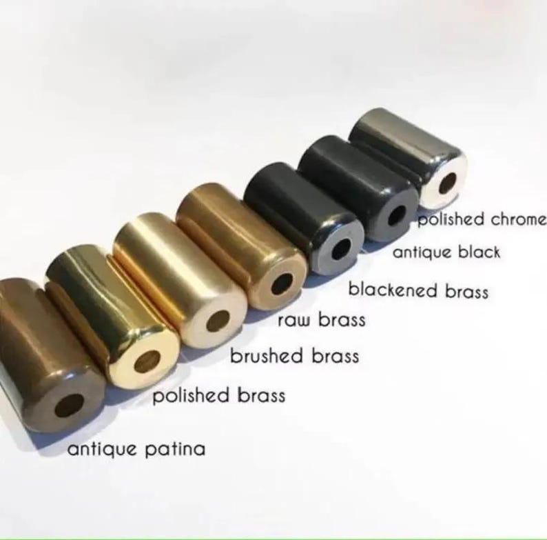 May include: A collection of cylindrical metal hardware samples in various finishes, including antique patina, polished brass, and polished chrome. Each cylinder has a hole through the center. The text labels the finishes: antique patina, polished brass, brushed brass, raw brass, blackened brass, antique black, and polished chrome.