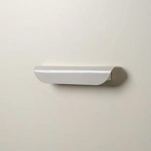 May include: A minimalist, light gray floating shelf. The shelf has a curved front edge and is mounted on a neutral-colored wall. The design is simple and modern, suitable for displaying small items or decor.
