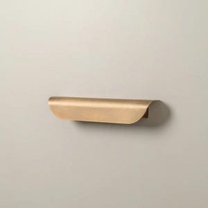May include: A curved, brass-colored shelf with a rounded front edge and a flat back. The shelf is mounted on a neutral-colored wall. The design is minimalist and modern, suitable for various decor styles.