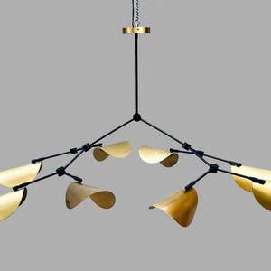 以下が含まれることがあります： 黒いフレームと金色の葉の形をしたシェードを備えたモダンなシャンデリア。チェーンから吊り下げられ、複数のアームが外側に伸びています。シェードは曲線的で、エレガントさを添えています。
