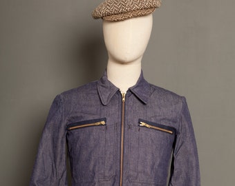 May include: A blue denim jacket with a zip fastening and two flap pockets on the chest. The jacket has a brown tweed newsboy cap on top.