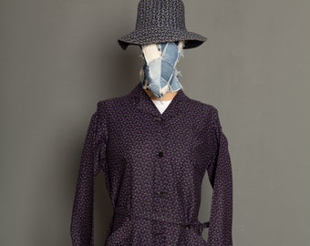 May include: A long-sleeved purple dress with a small floral print. The dress has a button-up front and a tie belt at the waist.