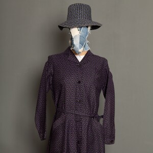 May include: A long-sleeved purple dress with a small floral print. The dress has a button-up front and a tie belt at the waist.