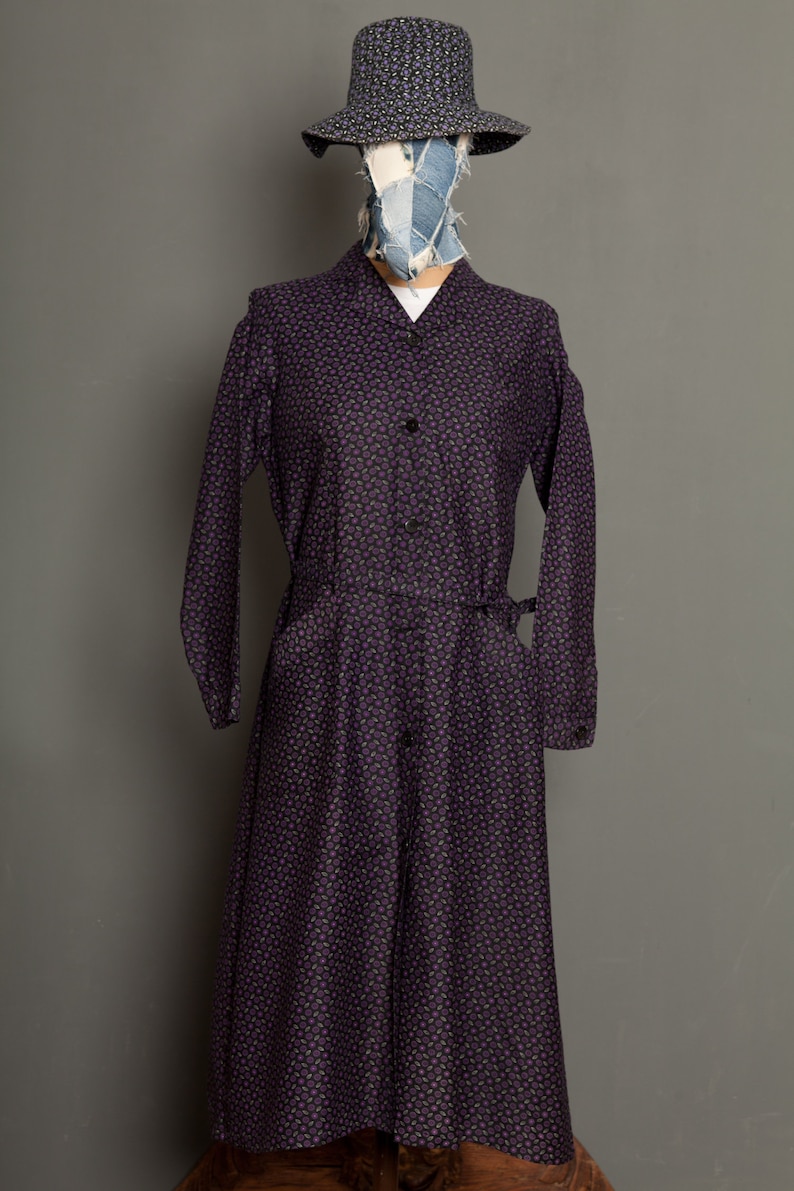 May include: A long-sleeved purple dress with a small floral print. The dress has a button-up front and a tie belt at the waist.