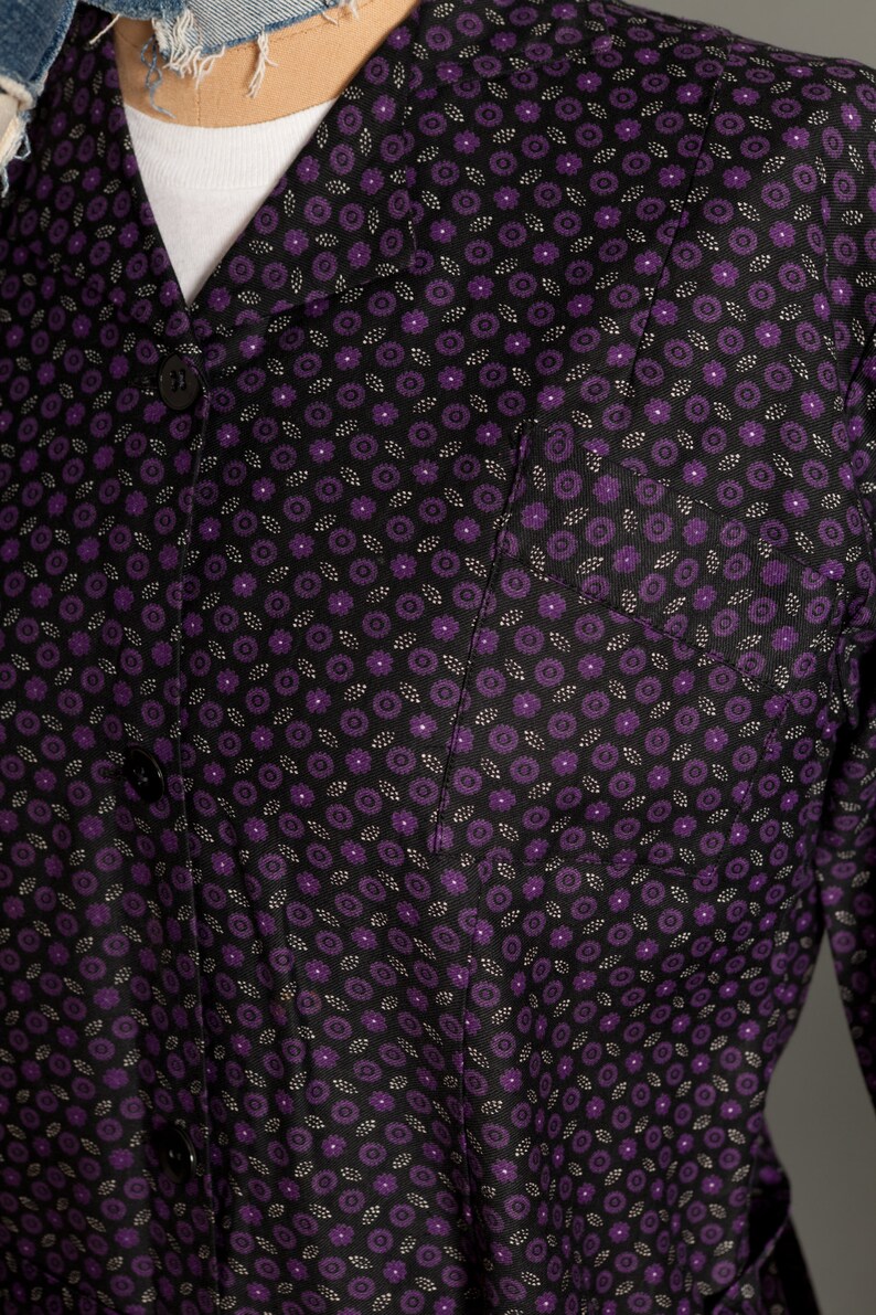 May include: A black button-up shirt with a purple floral pattern. The shirt has a collar and a pocket on the left side.