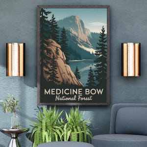 May include: A framed poster with the text "MEDICINE BOW National Forest" hangs above a blue armchair and ottoman. The poster depicts a mountain landscape with a lake and trees. Two gold and copper sconces flank the poster. A small silver side table and plants complete the scene.