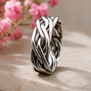 May include: A silver ring featuring a complex, interwoven design of multiple polished metal strands that overlap and twist around the entire circumference of the band, creating a textured, cage-like appearance with high-contrast highlights and shadows.