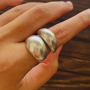 Puede incluir: Un anillo de plata con un diseño único. El anillo presenta dos bandas redondeadas, lisas y pulidas que se colocan una al lado de la otra. El anillo está hecho de un material metálico brillante.
