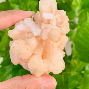 May include: A raw, pale peach-colored mineral specimen featuring a cluster of crystalline structures with a translucent, jagged surface texture. The formation displays irregular, blocky shapes and varying shades of light orange and white throughout.