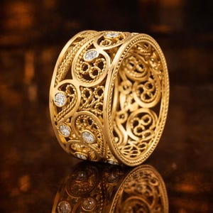May include: A gold ring with an intricate filigree design. The ring features a series of openwork patterns and is embellished with several small, round, clear gemstones. The ring's surface reflects light, highlighting its detailed craftsmanship.