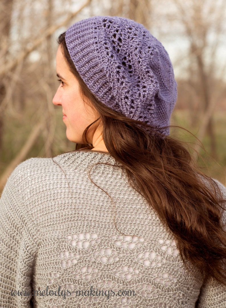 May include: A woman wearing a purple crocheted beanie with a lacy design. She is wearing a grey crocheted sweater with a lacy design on the back. The sweater has the text "www.melodays-makings.com" on the bottom.