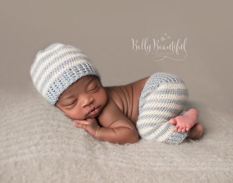 May include: A newborn baby wearing a blue and white striped crocheted hat and matching trousers, sleeping on a light brown fluffy blanket.
