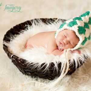 Può includere: Un neonato dorme in un cesto di vimini marrone rivestito di pelliccia sintetica bianca. Il bambino indossa un cappello all'uncinetto bianco e verde.