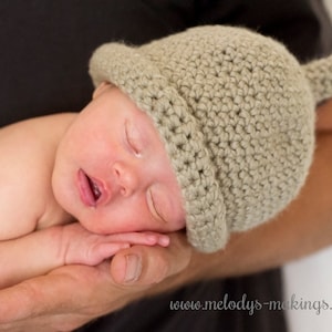 May include: A sleeping baby wearing a beige crocheted hat with a pointed top. The baby is lying on a person's arm.