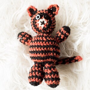 May include: A crocheted cat toy with black and orange stripes. The cat has black button eyes and a white nose.