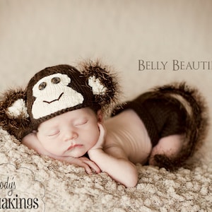 Może przedstawiać: Noworodek w brązowej czapce małpki i pasującej osłonie na pieluchę, leżący na miękkim, teksturowanym kocu. Czapka ma białą twarz i guziczkowe oczy. Widoczny jest tekst "Belly Beautiful" i "Melody's Makings".
