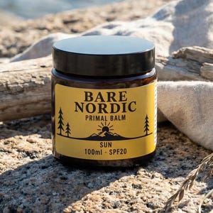 May include: A glass jar of Bare Nordic Primal Balm with a black lid. The yellow label features black text and a sun graphic. The jar contains 100ml of SPF20 balm. The jar is resting on a rock.
